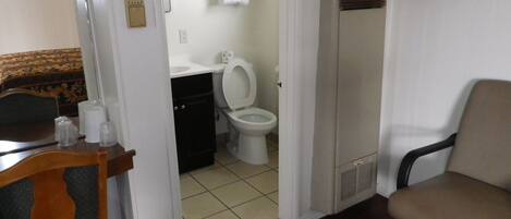 A small, compact room with a wooden chair, a small table, a toilet, and a cabinet.