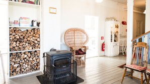 Une pièce avec une cheminée, des étagères à livres, un fauteuil en osier et un coin repas.