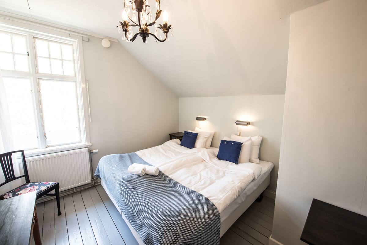 Une chambre à coucher avec un lit, une chaise, une table, une fenêtre et un lustre.