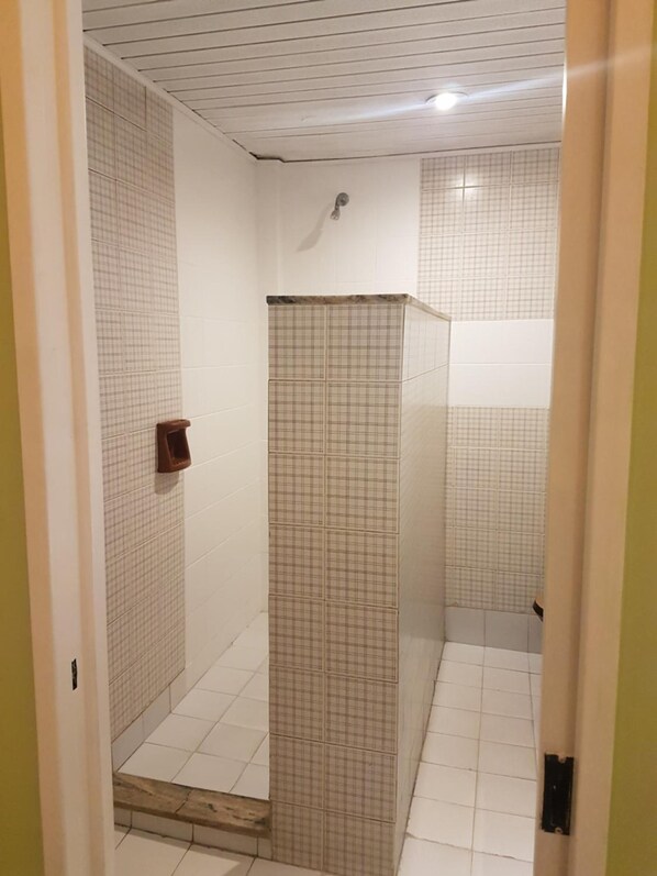 Un espacio de ducha pequeño y cerrado, con suelo y paredes de azulejos, un cabezal de ducha y un perchero para toallas.