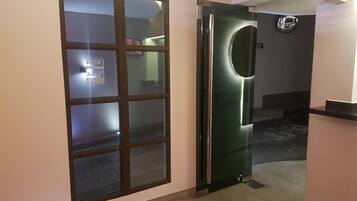 A hallway with a frosted glass door, a green door with a handle, and a sign on the wall.
