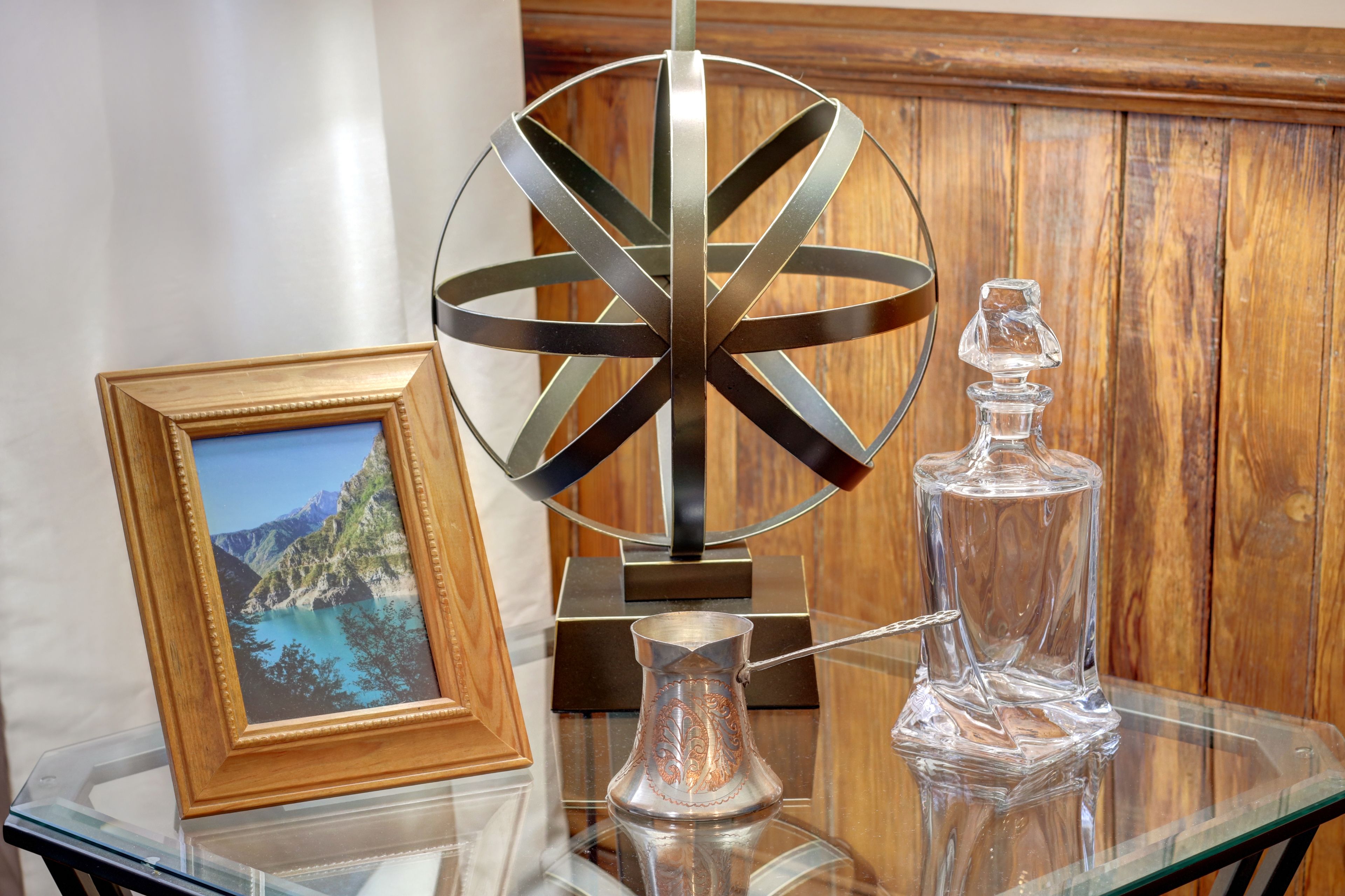 A glass table with a framed photograph, a metal sculpture, and a glass decanter.