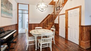 Un espace repas agrémenté d’un piano, d’un parquet, d’un lustre et d’un escalier.