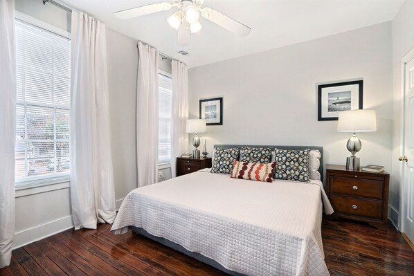 A bedroom with a large bed, two bedside tables with lamps, a ceiling fan, and two framed pictures on the wall. - Gallery Stays - Pop Collection (Savannah)