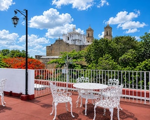 Eine Dachterrasse mit weißen schmiedeeisernen Stühlen und Tischen, einer Straßenlaterne und Blick auf ein historisches Gebäude mit Türmen.