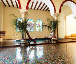 Un espace piscine doté d’un sol carrelé, de chaises longues en bois, de plantes en pot et d’une piscine avec un escalier en métal.