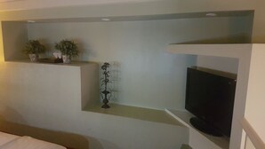 A room with a bed, a television mounted on a wall, and a small shelf with potted plants. - Uman Hotel (Motel) (Buenos Aires)