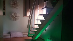 A modern staircase with a green-lit spiral design, a white bench, and decorative wall art. - Uman Hotel (Motel) (Buenos Aires)