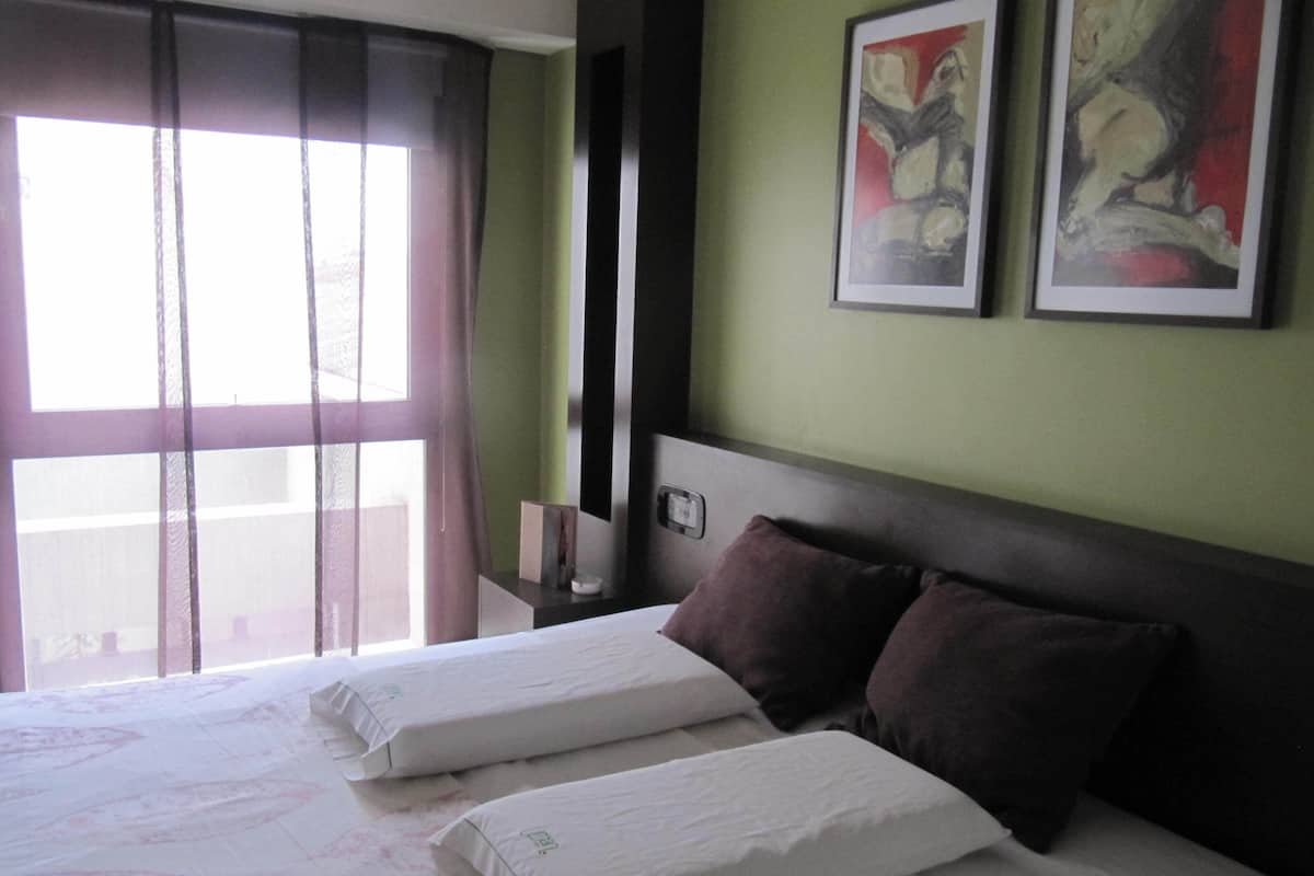 Una habitació d'hotel amb dos llits, un finestral gran amb cortines i dues obres d'art en marc a la paret.