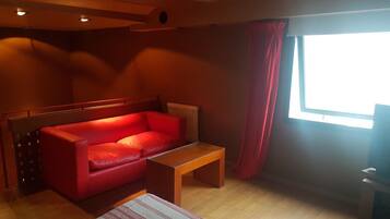 Um quarto com sofá vermelho, mesa de centro de madeira e tapete estampado.