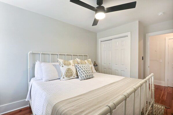 A bedroom with a bed, white walls, a ceiling fan, and a door. - Gallery Stays - Parkside Loft (Savannah)