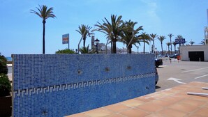 A blue tiled fence with palm trees and a clear sky in the background. - Les Doyes Bl 4 pta 145 (Peñiscola)