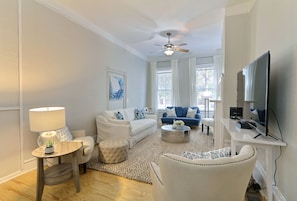 Una sala de estar moderna con un sofá blanco, un sofá azul, una mesa de centro redonda y un televisor sobre un mueble.