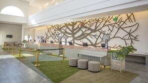 Un área de recepción de diseño moderno, con un gran mural de ramas de árboles, mostrador de recepción y una zona de estar con otomanas.