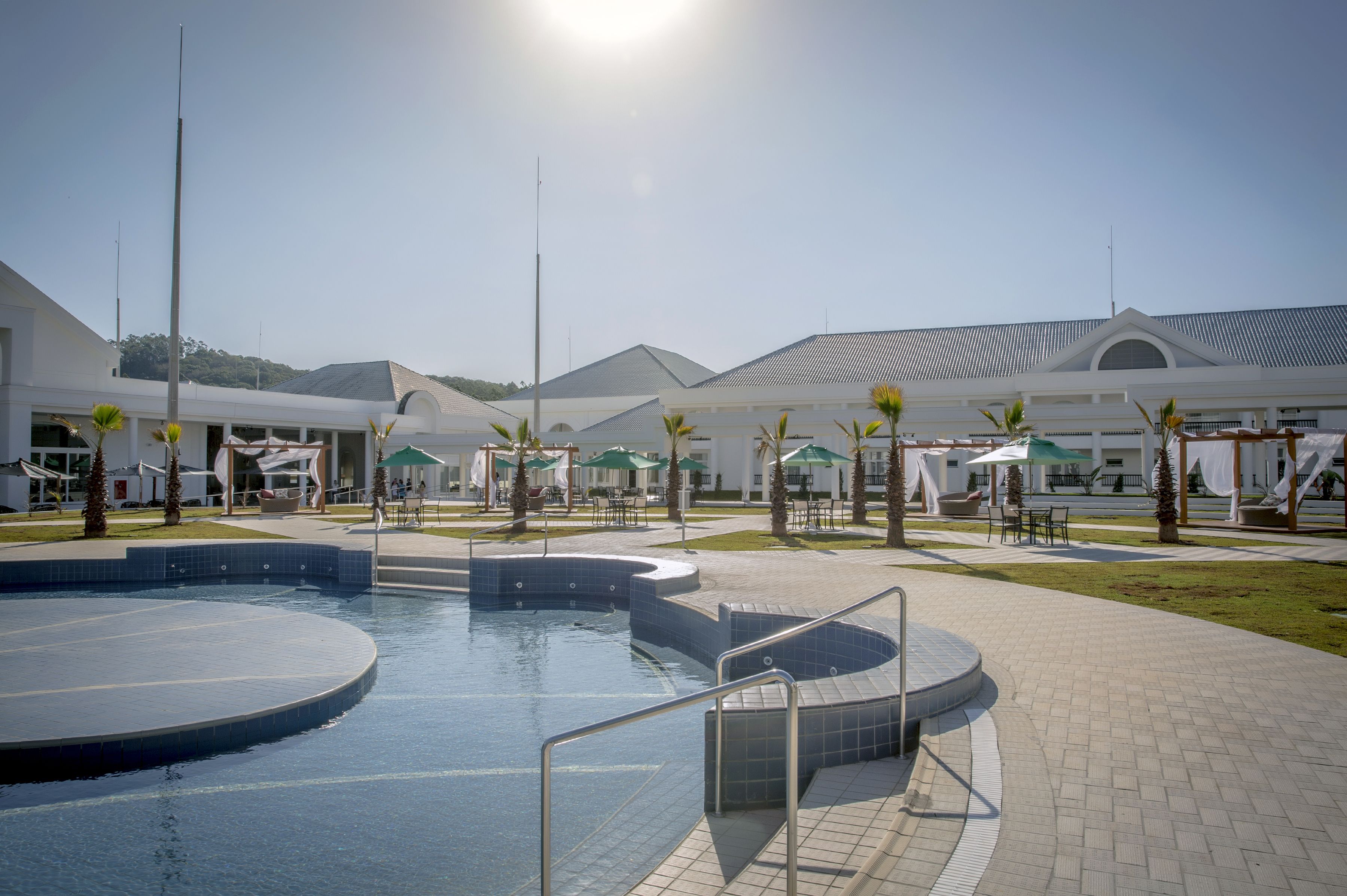 Uma área de piscina com uma piscina circular, uma cobertura de sombra e um edifício de design moderno.