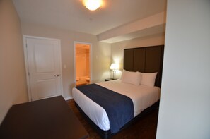Une chambre d’hôtel comprenant un lit, une table de chevet, une commode, une lampe et une porte donnant accès à une salle de bain.