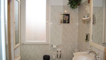 Un baño con inodoro, lavamanos y espejo. Hay una ventana con vistas al exterior.