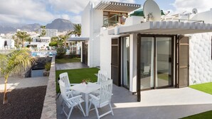 Eine moderne Terrassengruppe im Freien mit weißem Tisch und Stühlen, ein kleiner Garten und ein Pool im Hintergrund.