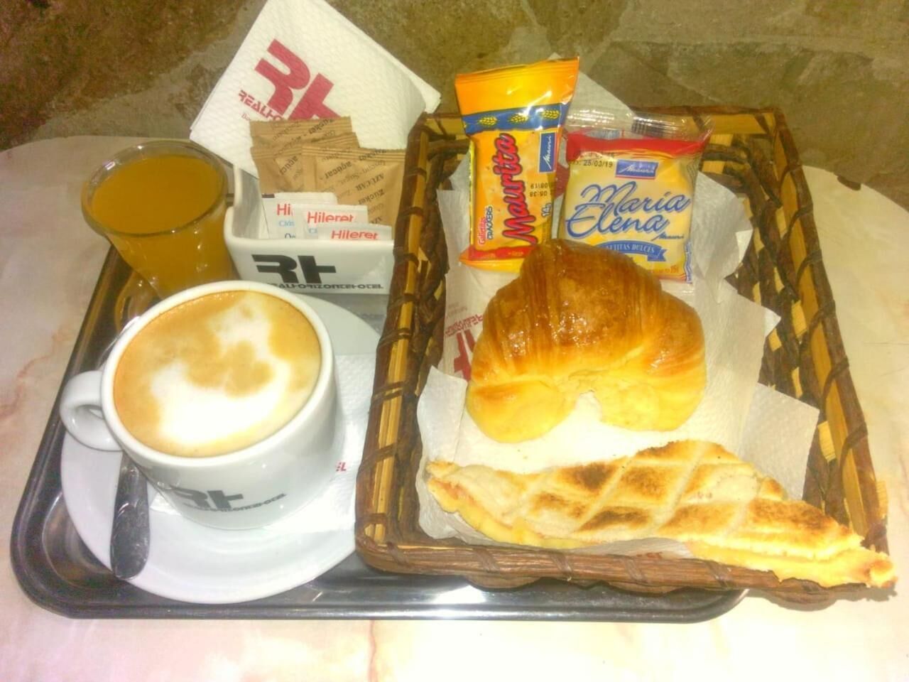 Una bandeja con una taza de café, un croissant, un muffin y algunos bocadillos.