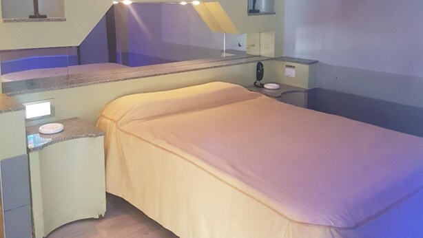 Habitación de hotel con cama, escritorio, silla, mesita pequeña y mesita de noche.