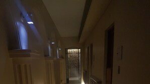 Un pasillo tenuemente iluminado, con un radiador a la izquierda y una barandilla de madera a la derecha.
