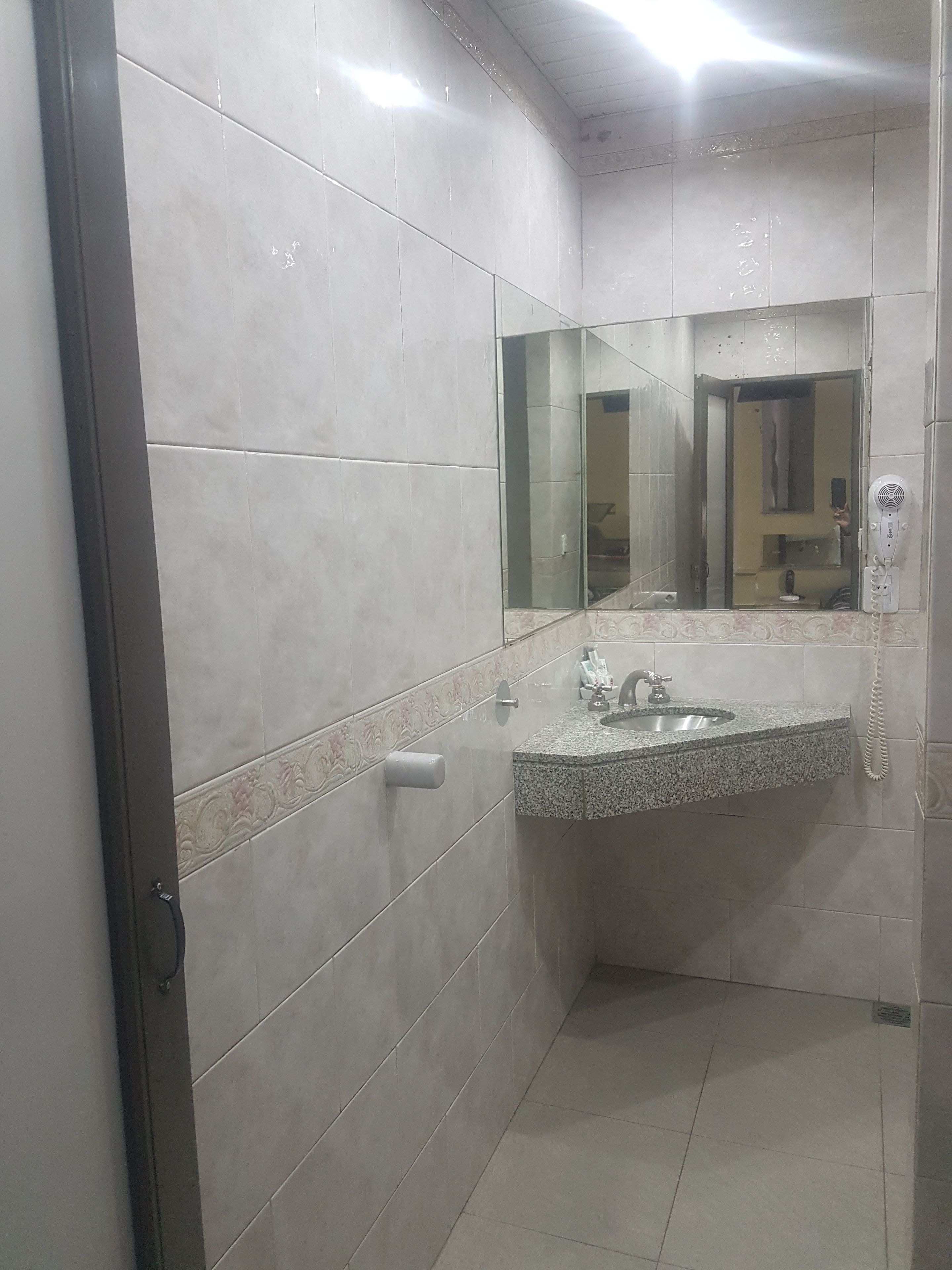 Casa de banho com lavatório, espelho e secador de cabelo na parede.