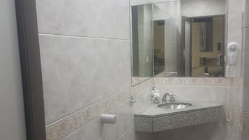 Casa de banho com lavatório, espelho e secador de cabelo na parede.