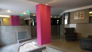 A lobby with a reception desk, a pink column, a seating area with a chair, and a small decorative water feature. - Dallas Hotel (Motel) (Buenos Aires)