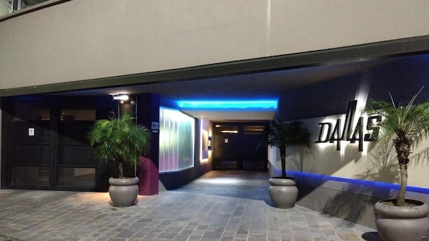 A hotel entrance with a "DALLAS" sign, potted plants, and a tiled walkway. - Dallas Hotel (Motel) (Buenos Aires)