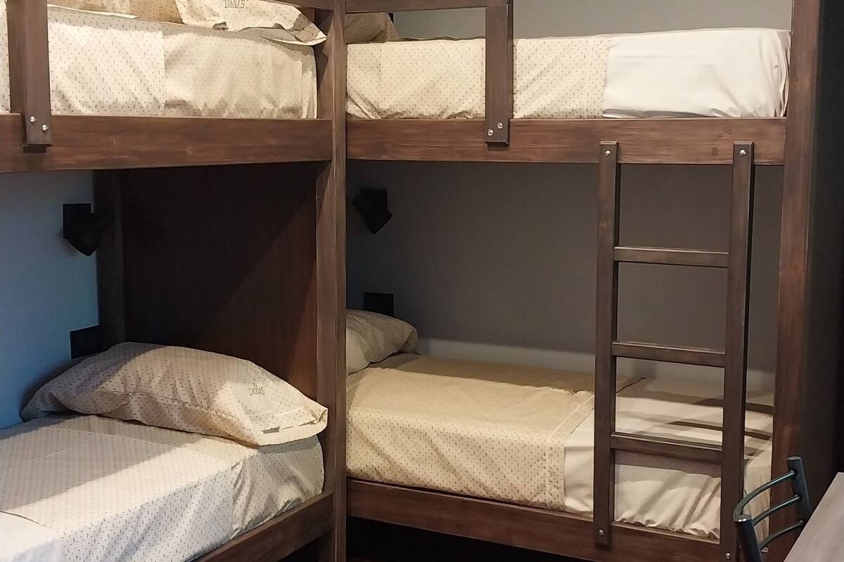 A bunk bed room with wooden headboards, a herringbone-patterned wooden floor, and a small window.