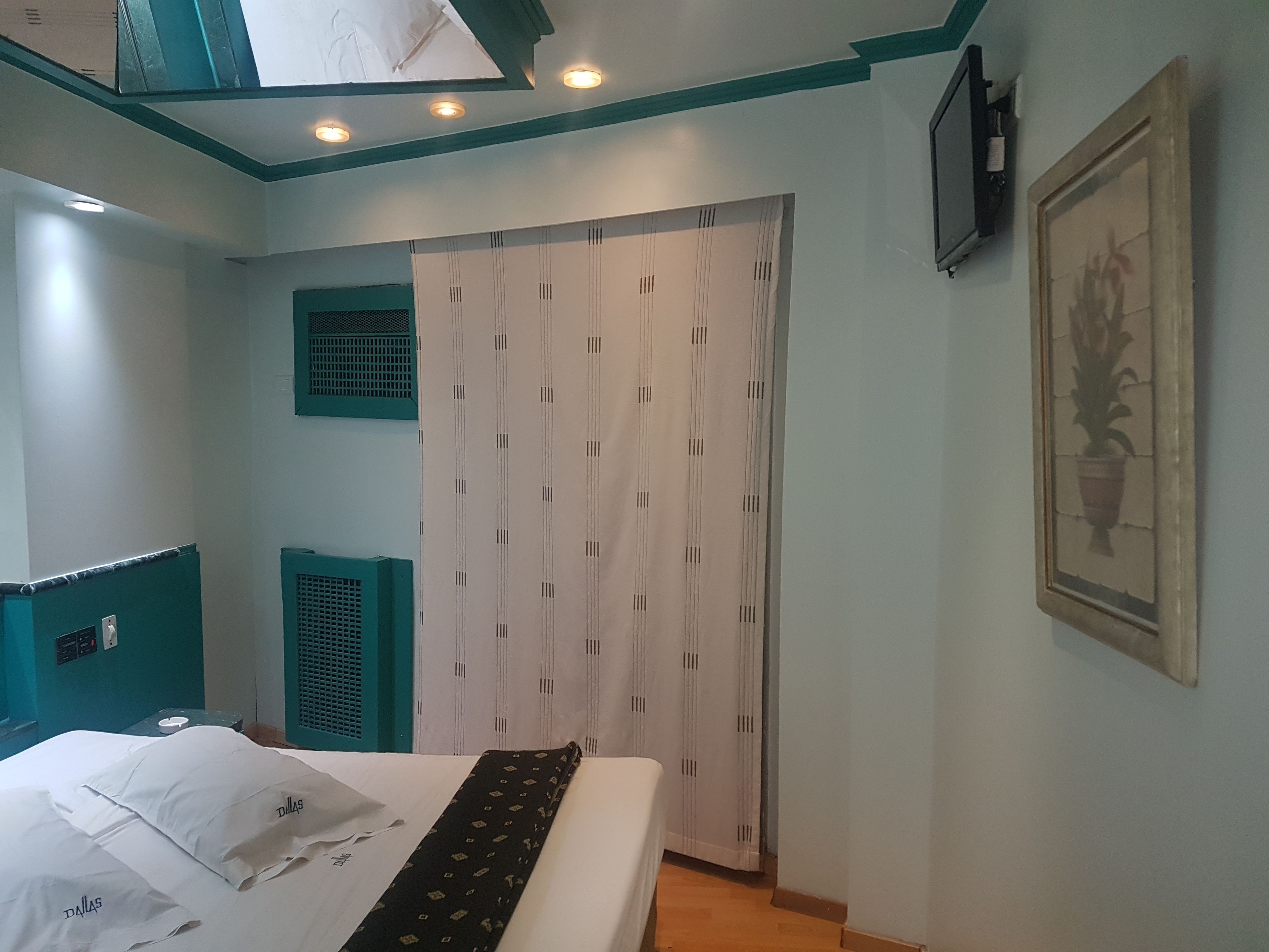 A bedroom with a bed, a wardrobe, a window, and a wall-mounted TV.