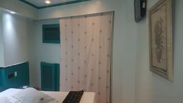 A bedroom with a bed, a wardrobe, a window, and a wall-mounted TV.