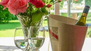A table with a glass vase of pink roses, two wine glasses, and a metal bucket containing a bottle of wine. - Cedar House Boutique B&B (Christchurch)