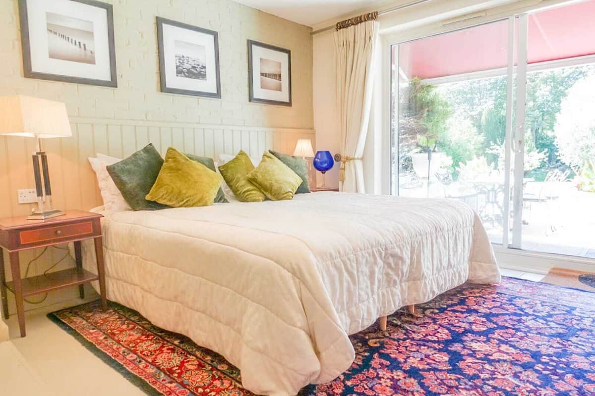 A bedroom with a large bed, a nightstand, a lamp, and a window with curtains.