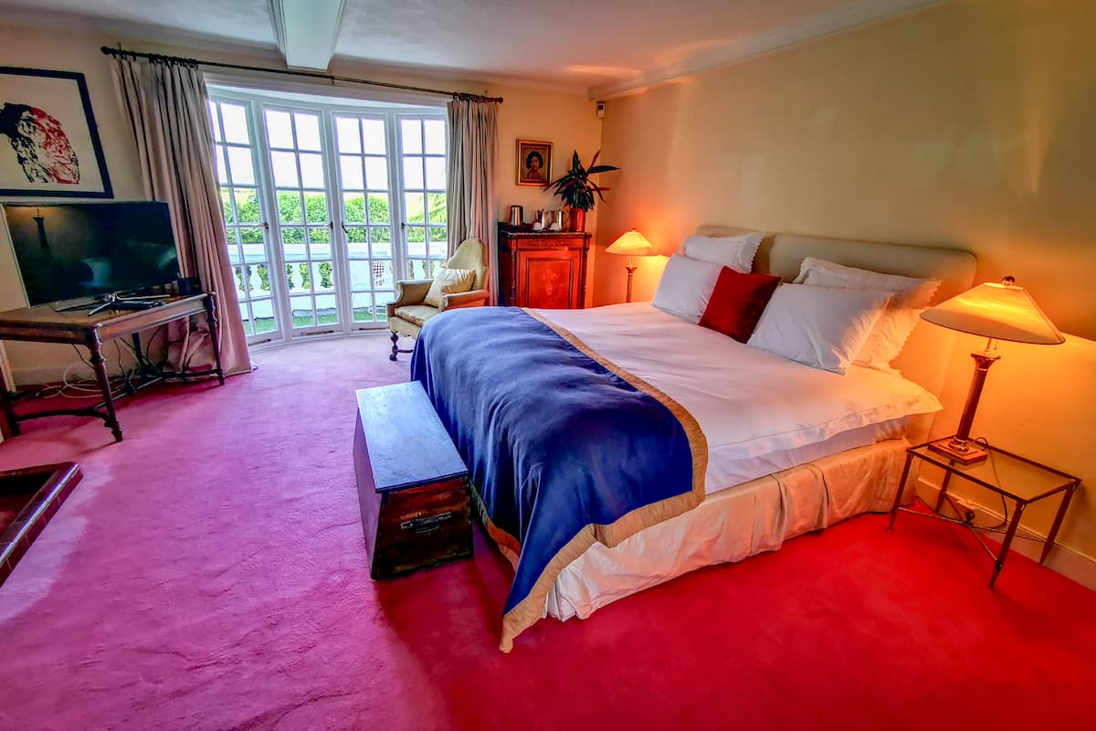 A bedroom with a large bed, a TV, a desk, and a bench.