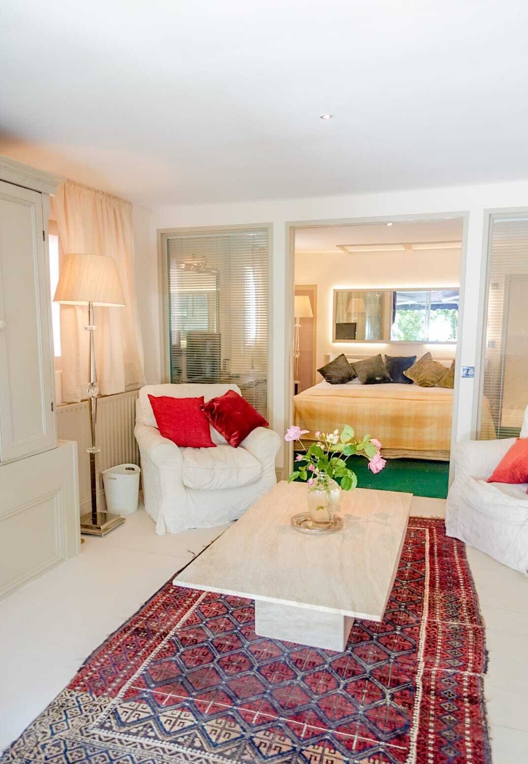 Una habitación bien iluminada con un sofá blanco, almohadas rojas, una mesita de café y una alfombra estampada.
