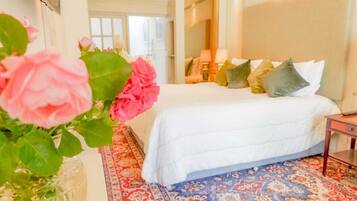 A hotel room with a bed, a nightstand, a vase with flowers, and a patterned rug.