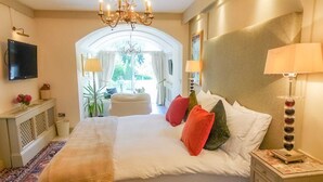 A hotel room with a large bed, a chandelier, a TV mounted on the wall, and a view of the outdoors through a window. - Cedar House Boutique B&B (Christchurch)