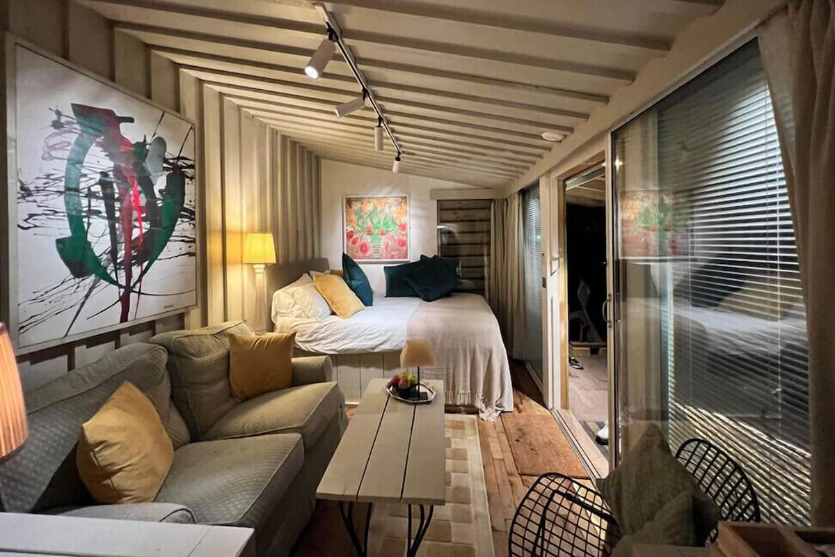 A modern, compact room with a bed, a sofa, a small table, and a painting on the wall.