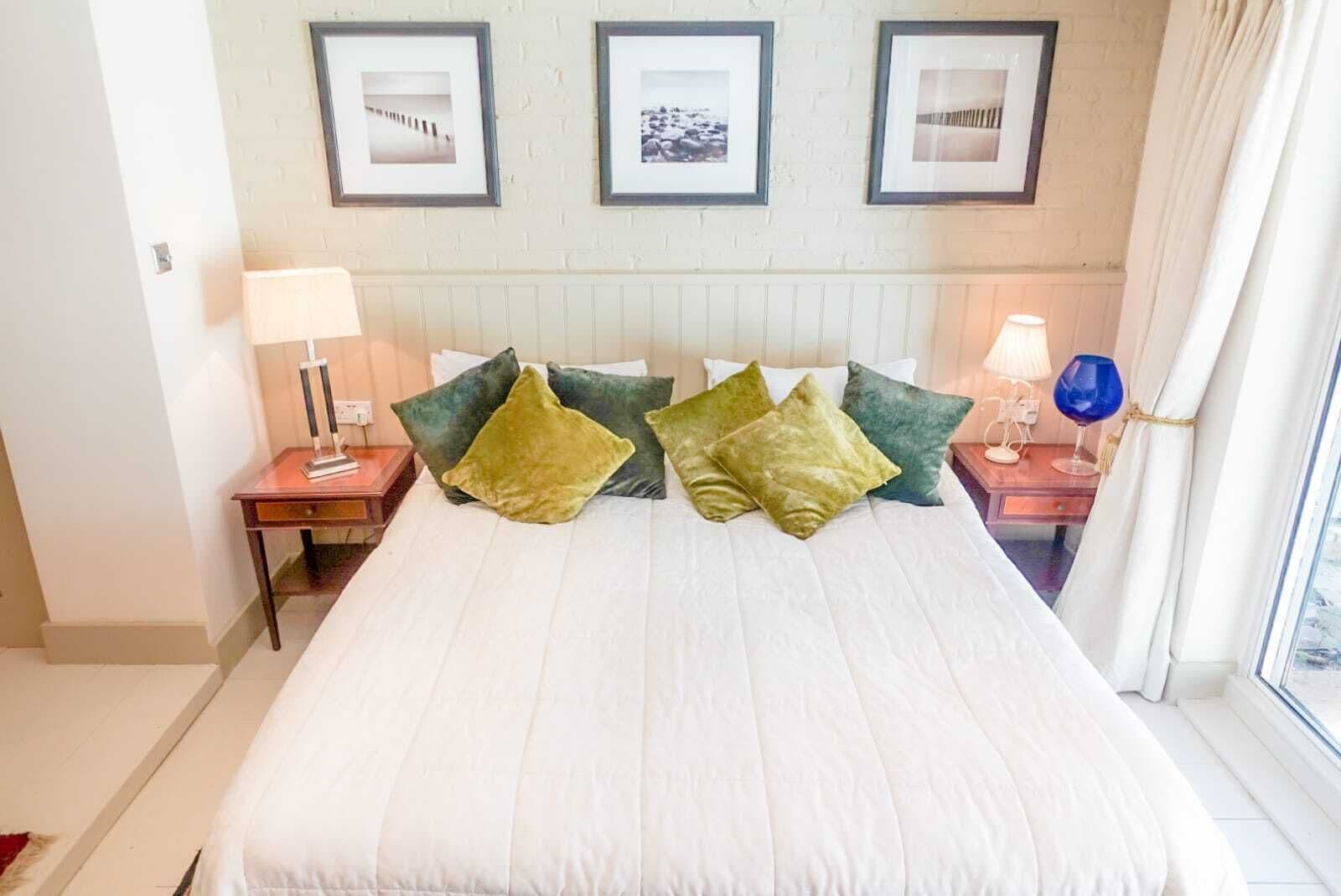 A hotel room with a large bed, two bedside tables, a window with curtains, and three framed pictures on the wall.