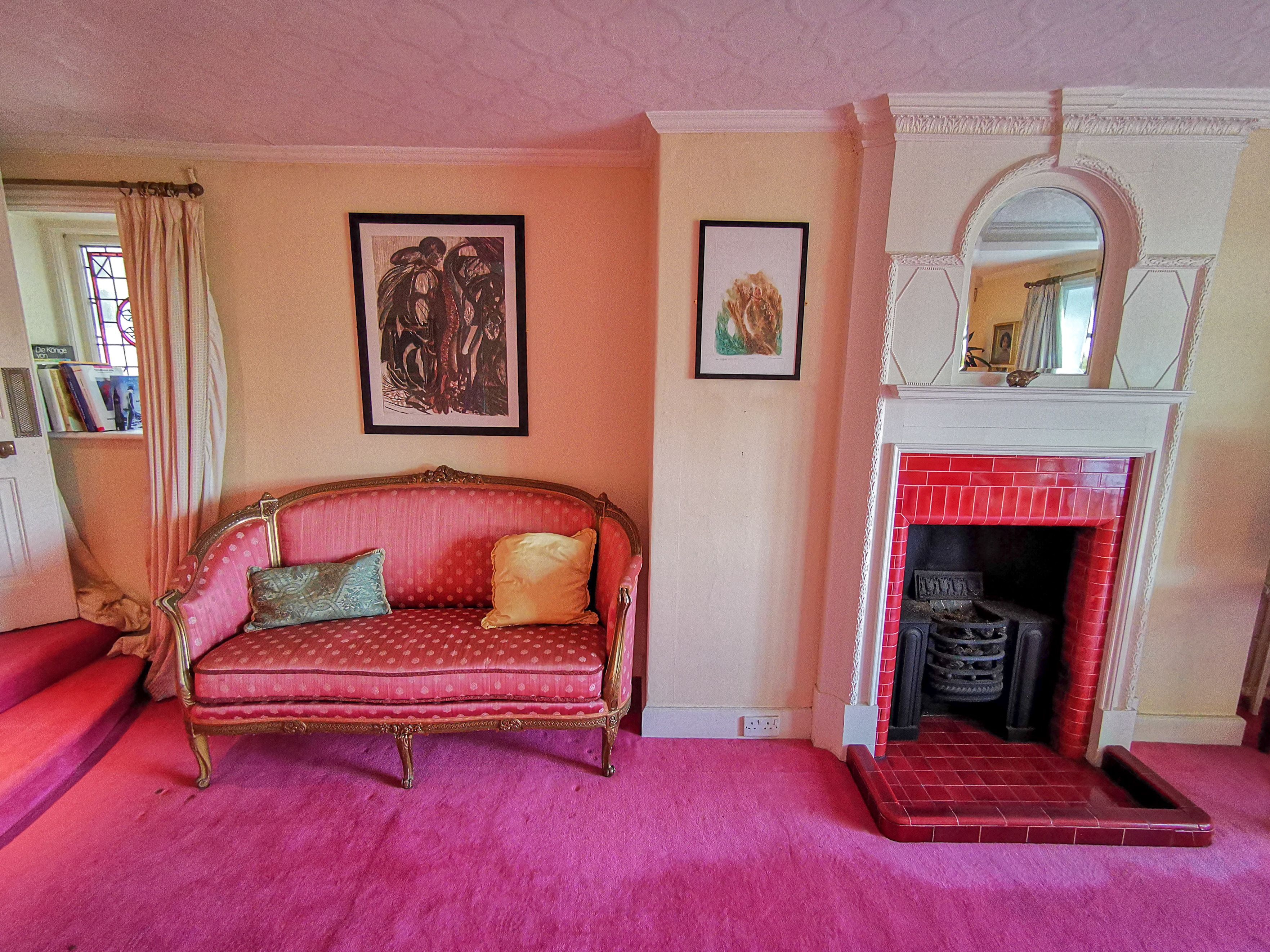 A room with a red sofa, a fireplace, and framed artwork on the walls.
