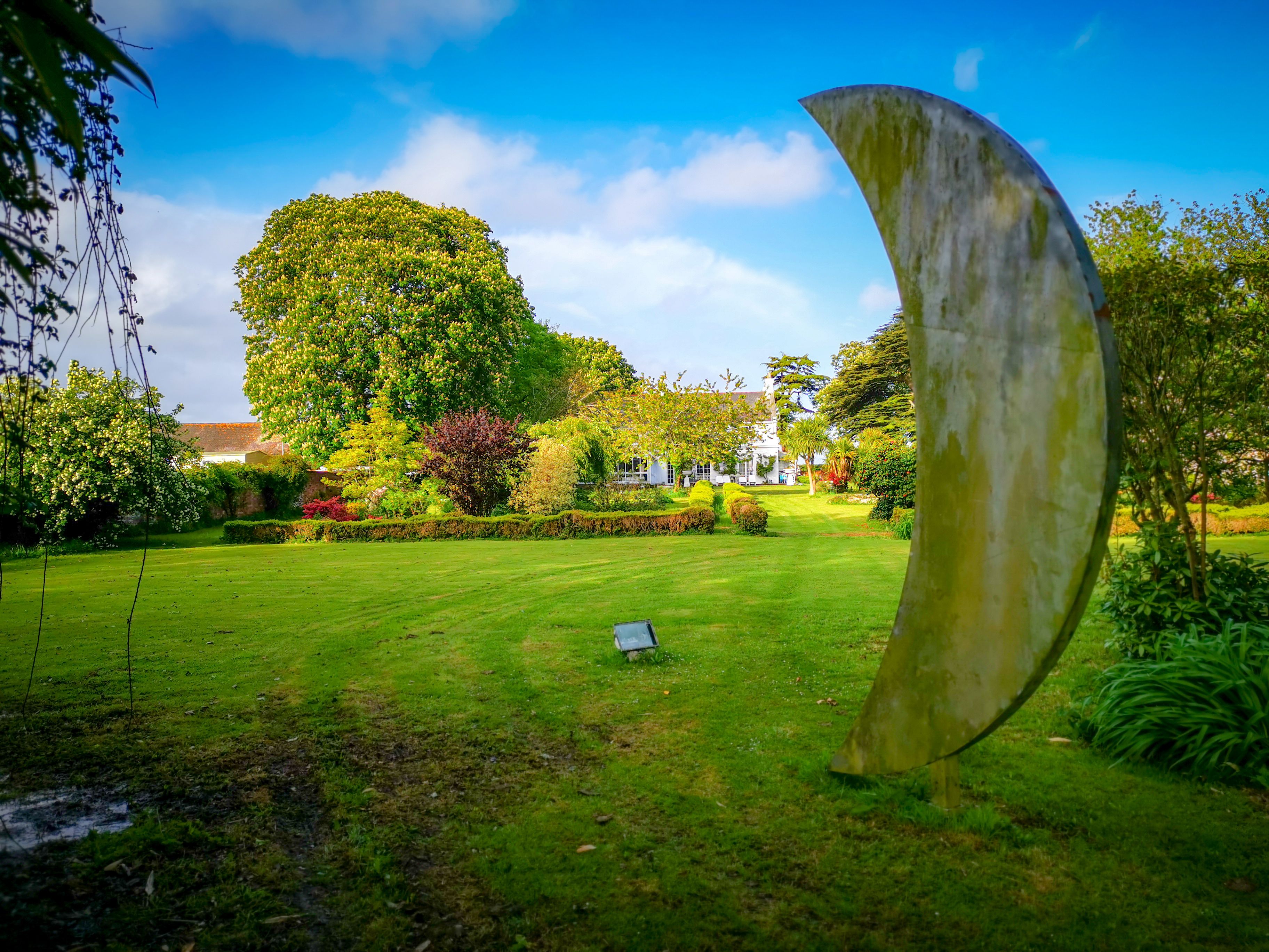 A garden with a large metal sculpture, a lawn, and a building in the background.