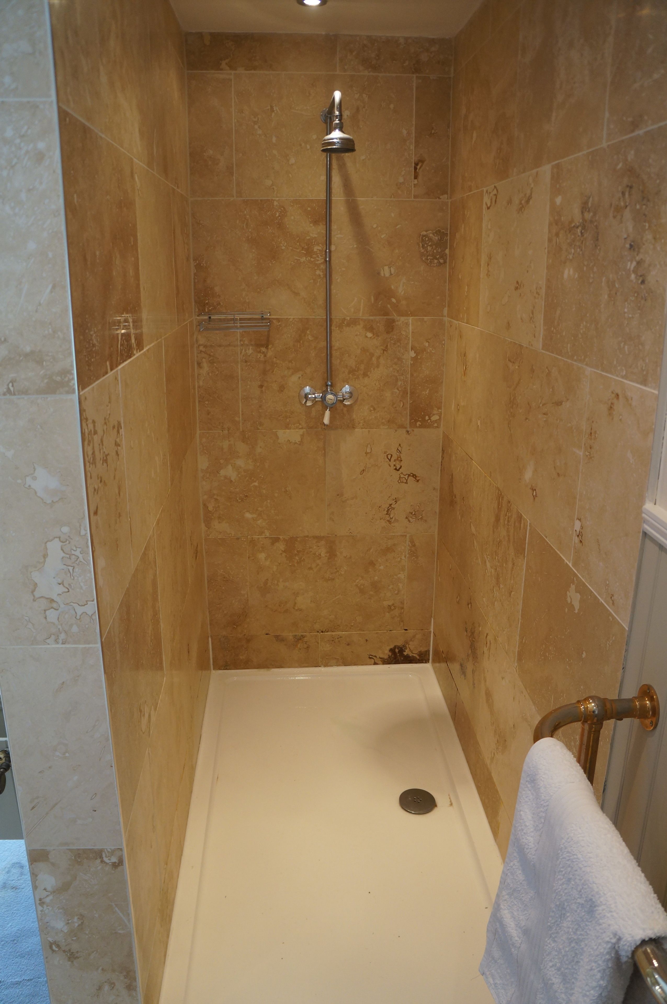Une cabine de douche équipée d’un pommeau de douche à main, d’un porte-serviettes et d’un drain.