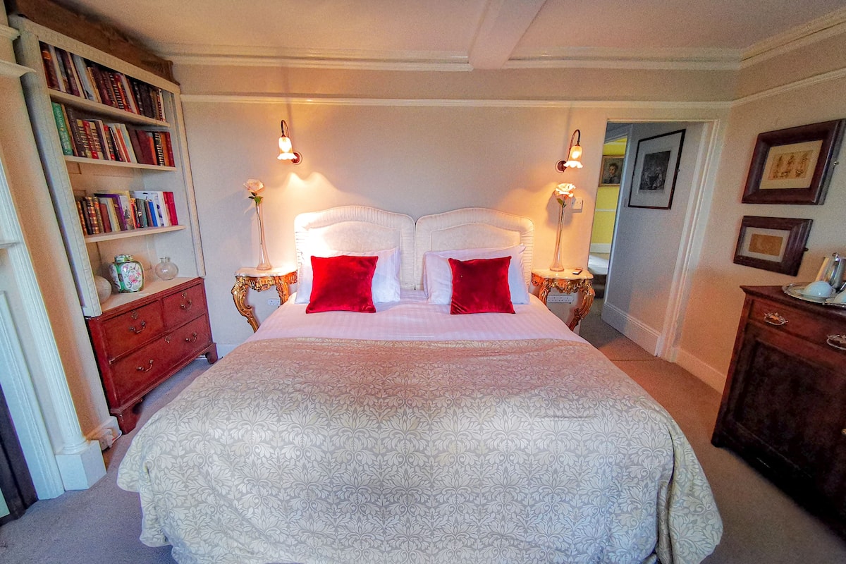 A neatly arranged bedroom with a large bed, two bedside tables with lamps, a bookshelf, and a framed picture on the wall.
