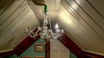 A room with a sloped ceiling, a chandelier, a chair, a bed, and framed pictures on the wall.