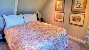 A bedroom with a bed, a nightstand, a lamp, and framed pictures on the wall.