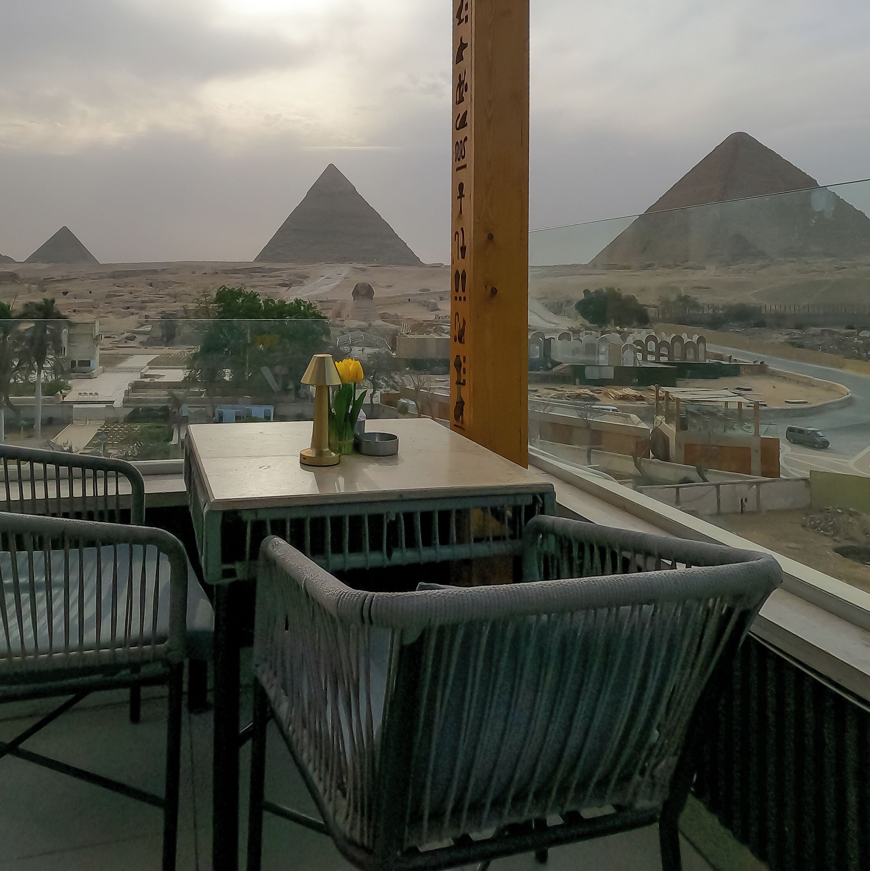Een balkon met uitzicht op de piramides, een tafel met een bloevas, en een stoel.