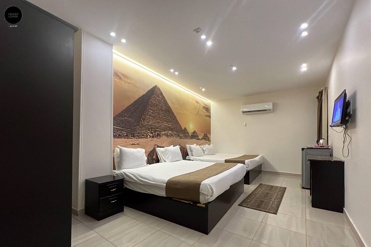 Una habitación de hotel moderna con una cama grande, un escritorio, un televisor de pantalla plana y un mural de una pirámide.