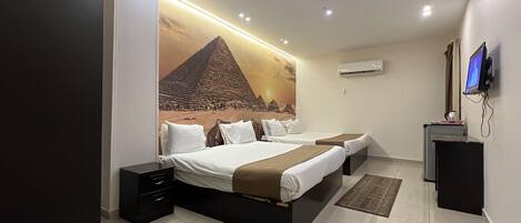 A modern hotel room with a large bed, a desk, a flat-screen TV, and a mural of a pyramid.