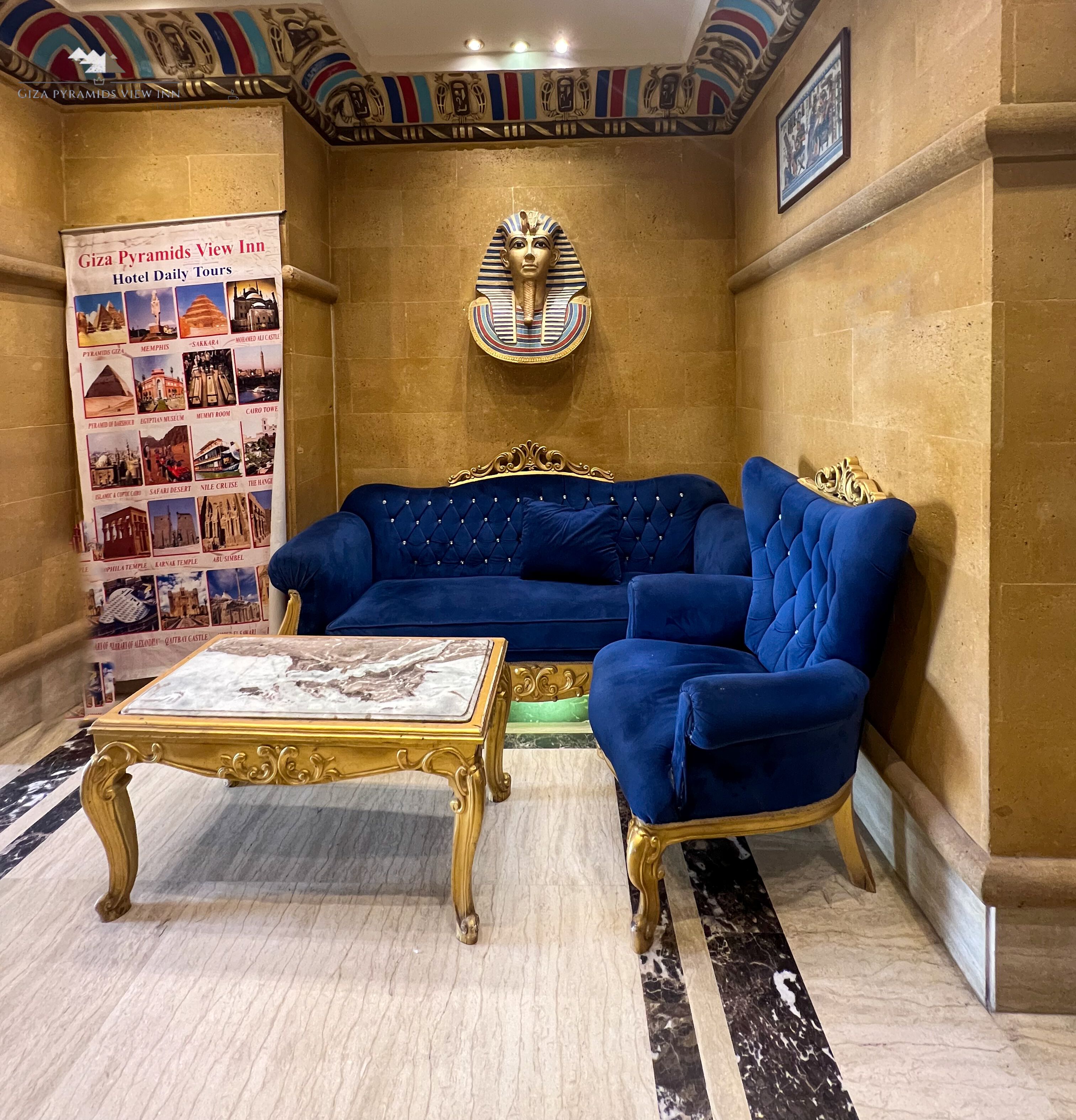 A lobby with a blue sofa, a gold-framed coffee table, and a wall-mounted Egyptian artifact. A banner with hotel information is visible.